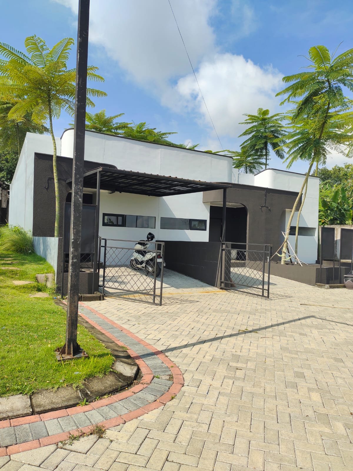 Rumah minimalis modern 1 lantai bernuansa hitam putih dengan carport, kanopi, pagar besi, dan halaman paving block.